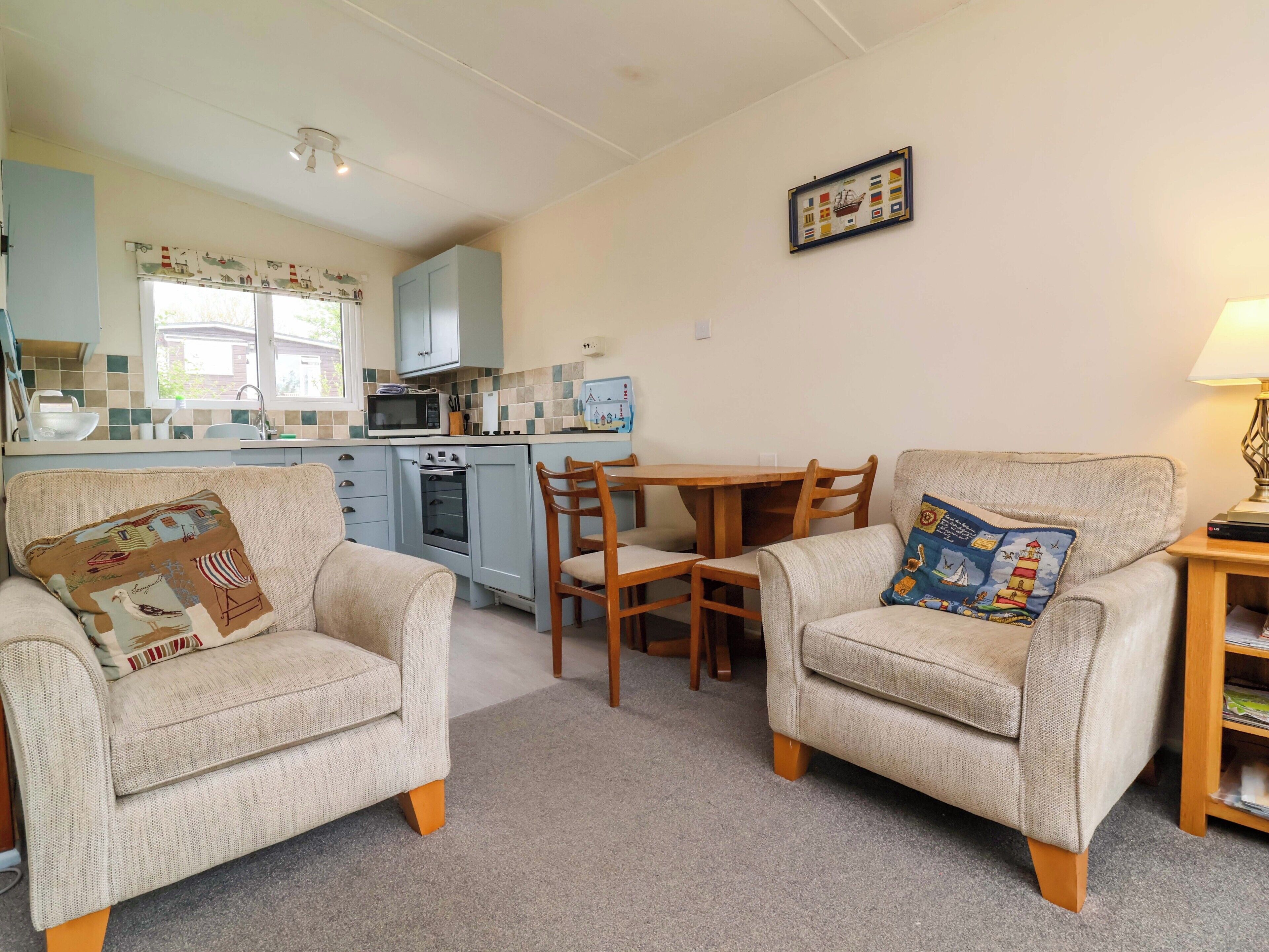A cozy living room with two armchairs, a wooden table, and a kitchen area with a microwave and oven.