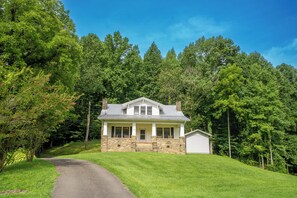 A two-story house with a stone foundation and a small attached garage, surrounded by dense forest. - 🌄 The Farmhouse at Foothills Farm 🌲 1930s Farmhouse, Creek & Hot Tub (Cosby)