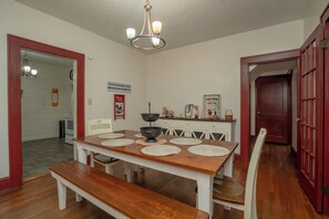 Uma sala de jantar com uma mesa de madeira, cadeiras brancas, um banco e um candelabro.