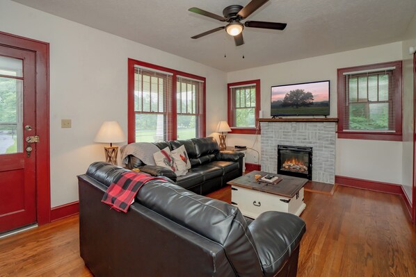 A living room with a fireplace, a sofa, a coffee table, and a television. - 🌄 The Farmhouse at Foothills Farm 🌲 1930s Farmhouse, Creek & Hot Tub (Cosby)