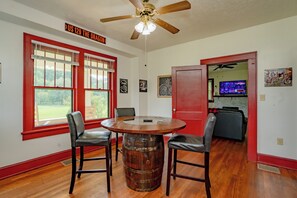 Um quarto com uma mesa redonda de madeira, duas poltronas de couro, um ventilador de teto e uma porta vermelha.