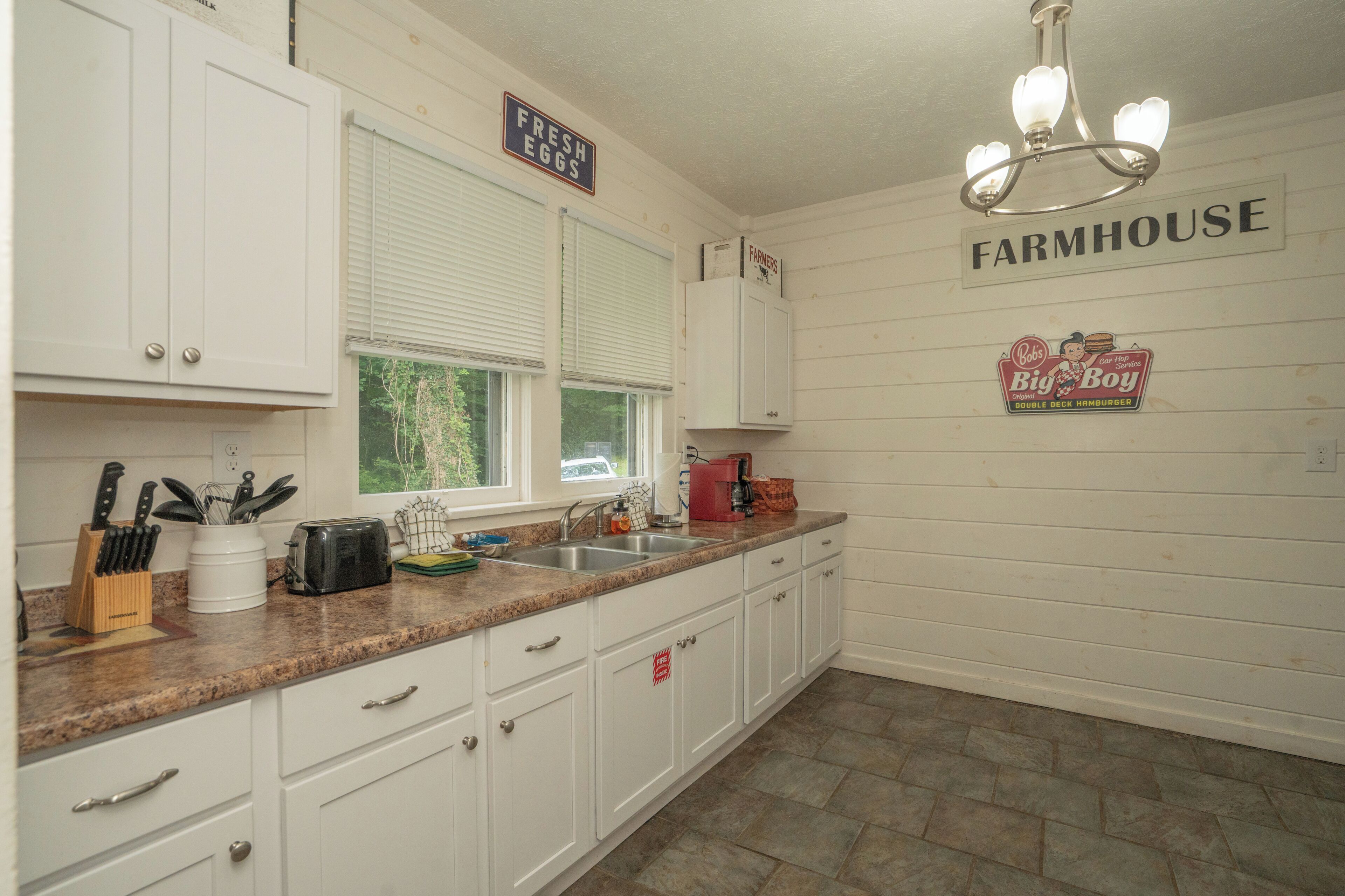 A kitchen with white cabinets, a granite countertop, a sink, and a chandelier.