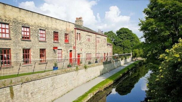 A stone building with red doors and windows, a canal beside it, and a fence. - *G11H* for a cosy luxurious lovely stay + Free Parking + Free Fast WiFi perfect for work or pleasure (West Yorkshire)