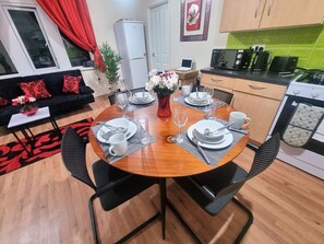 A dining area with a round table set for four, a sofa with red cushions, a refrigerator, a laptop, and a kitchen area with a stove and coffee maker. - *G11H* for a cosy luxurious lovely stay + Free Parking + Free Fast WiFi perfect for work or pleasure (West Yorkshire)