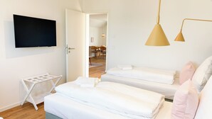 Habitación de hotel con dos camas, un televisor, un tendedero y un área de comedor visible a través de una puerta abierta.