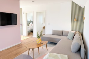 A modern living room with a flat-screen TV, a sofa, a coffee table, and a striped wall. - Tower of Power – Balcony, Fireplace, Upper Floor, Washing Machine, Private Parki (Olpenitz)