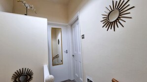 Un couloir avec une porte blanche, un miroir et deux miroirs décoratifs en forme de soleil fixés au mur.