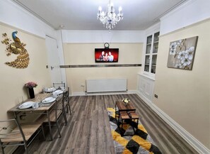 A dining area with a long table set for four, a chandelier, a television, and a peacock wall decoration. - *6R*your most amazing & relaxed stay + Free Parking + Free Fast WiFi * (Holbeck)