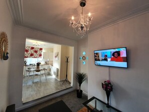 A living room with a TV, a chandelier, a potted plant, and a dining area visible through an open door. - 12JT* king bed cosy and lovely house + Free Parking + Free Fast WiFi (Morley)