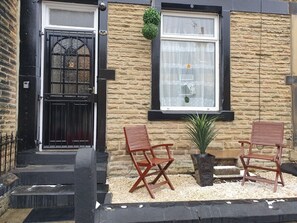 A building entrance with a black door, two wooden chairs, a potted plant, and a window with a curtain. - 12JT* king bed cosy and lovely house + Free Parking + Free Fast WiFi (Morley)