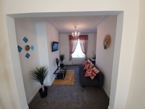 A living room with a sofa, a coffee table, a TV, and a window with curtains. - 12JT* king bed cosy and lovely house + Free Parking + Free Fast WiFi (Morley)