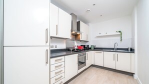 A modern kitchen with white cabinets, stainless steel appliances, and a black countertop. - Sleep Well - Modern Apartment for 4 near Stations (London)