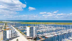 Een jachthaven met talloze boten afgemeerd, moderne gebouwen met balkons, en een helder uitzicht op zee en de verre kustlijn.