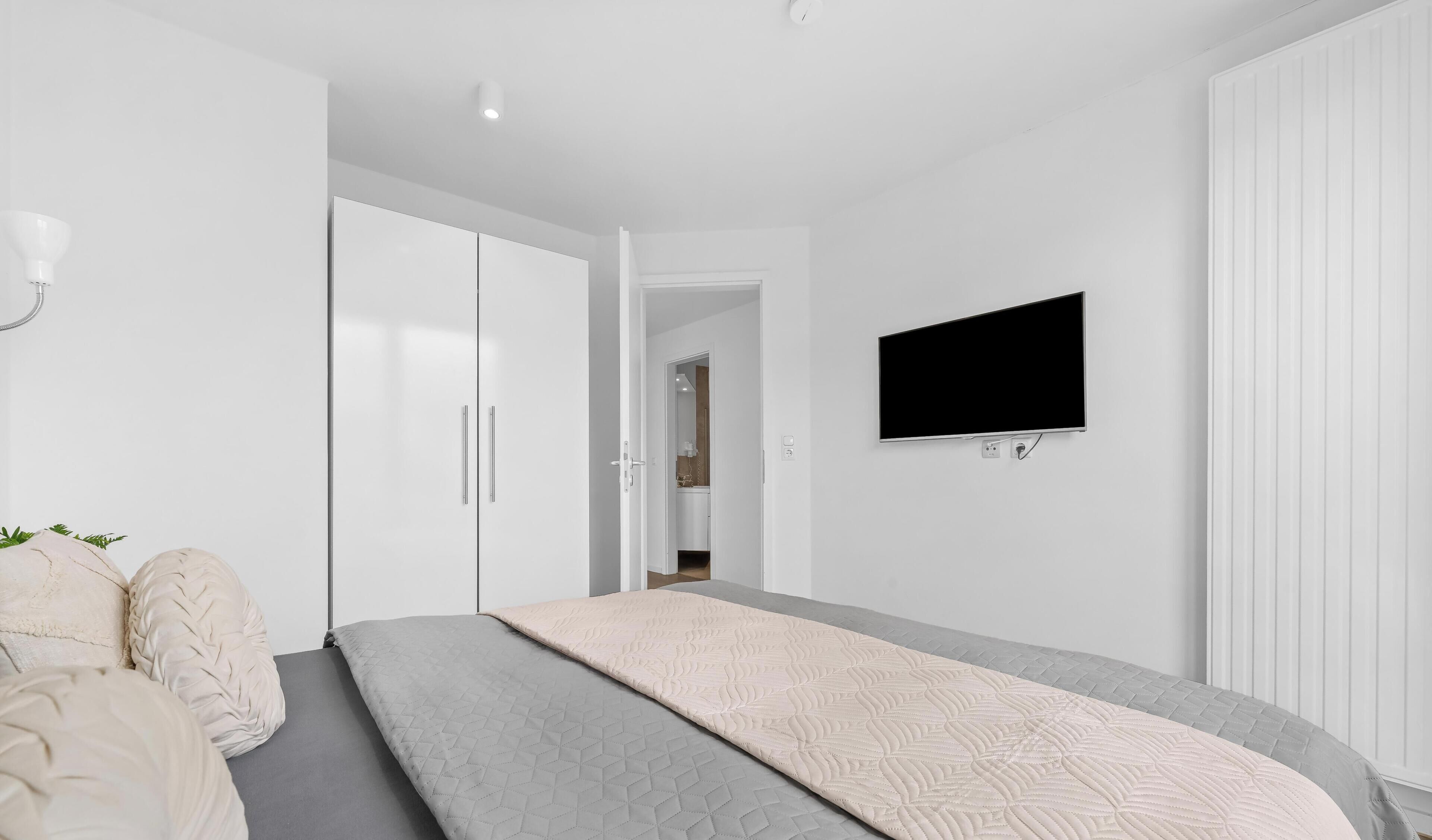 A modern bedroom with a bed, a TV mounted on the wall, and a wardrobe.