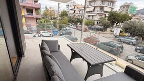 A balcony with a sofa and table, overlooking a street with parked cars and buildings. - Alimos Urban Retreat (Alimos)