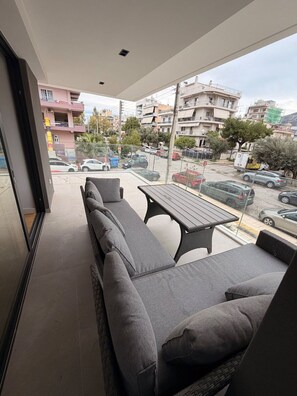 Uma varanda com sofá e mesa, com vista para uma rua com carros estacionados e edifícios.