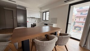 A modern kitchen with white cabinets, a wooden dining table, and two grey chairs. - Alimos Urban Retreat (Alimos)