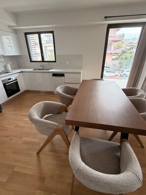 A modern kitchen with white cabinets, a wooden dining table, and six grey upholstered chairs.