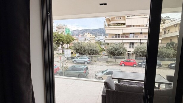 A room with a sliding glass door leading to a balcony with a view of a parking area and buildings. - Alimos Urban Retreat (Alimos)