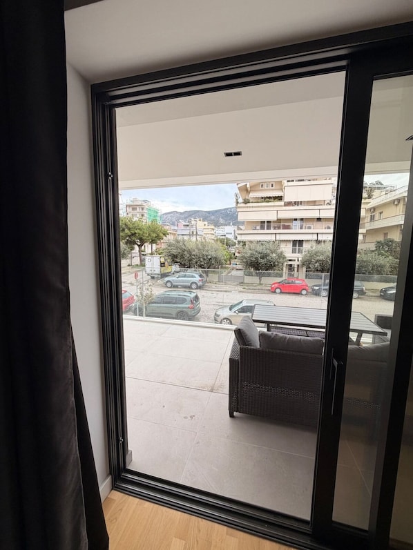 Une pièce dotée d’une porte-fenêtre coulissante donnant sur un balcon avec vue sur un parking et des immeubles.