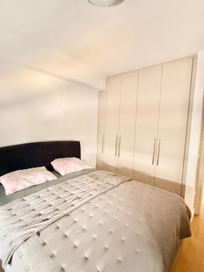 A bedroom with a bed, a headboard, a wardrobe, and a bedside table.