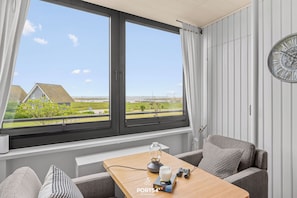 Ein Zimmer mit einem großen Fenster, einem Tisch mit Kaffeemaschine, einer Couch und einer Uhr an der Wand.