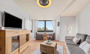 Ein modernes Wohnzimmer mit Flachbildfernseher, Holzmöbeln, einem Couchtisch mit einer Vase und einer Couch.