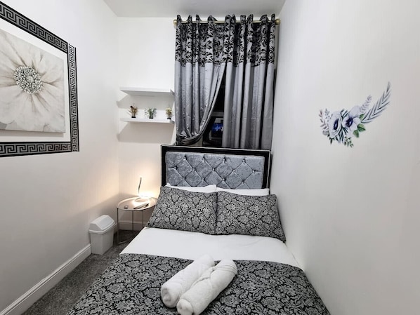 A small, neatly arranged bedroom with a bed, bedside table, and a nightstand.