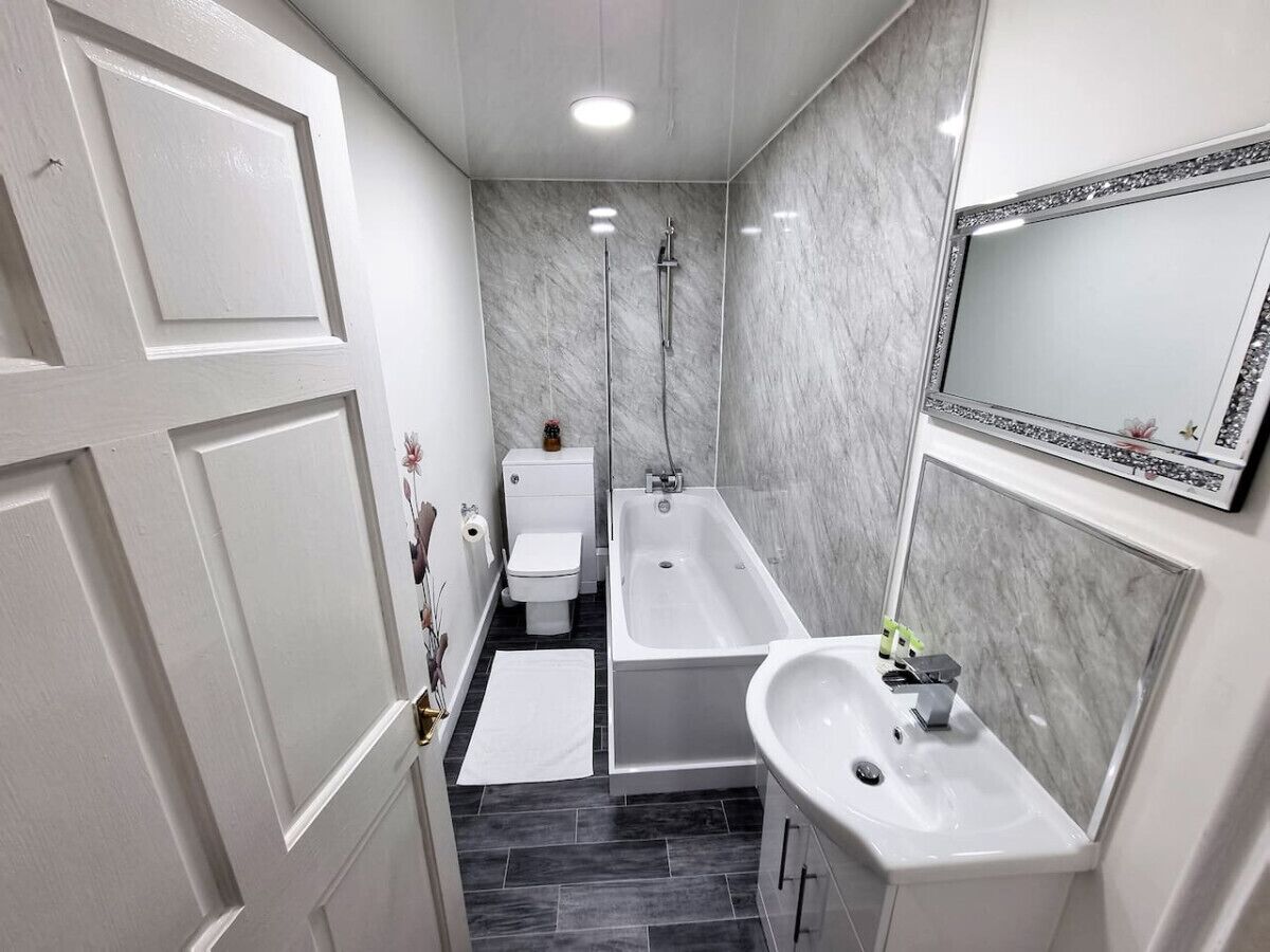 Ein modernes Badezimmer mit Toilette, Badewanne und Waschbecken, Marmorwänden und einer Tür mit dekorativer Verkleidung.