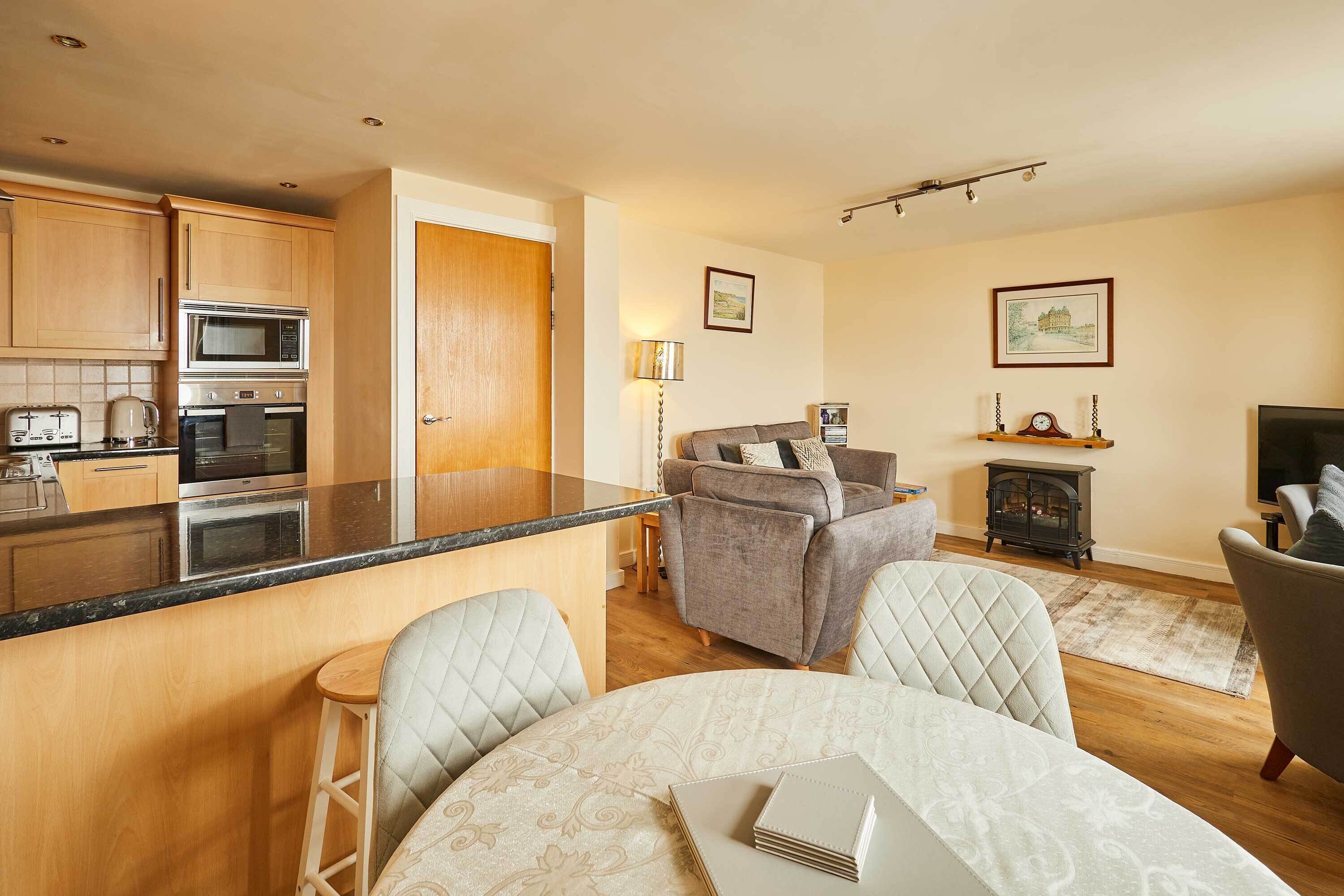 A modern kitchen with a central island, a dining area with a table and chairs, a sofa, and a fireplace.