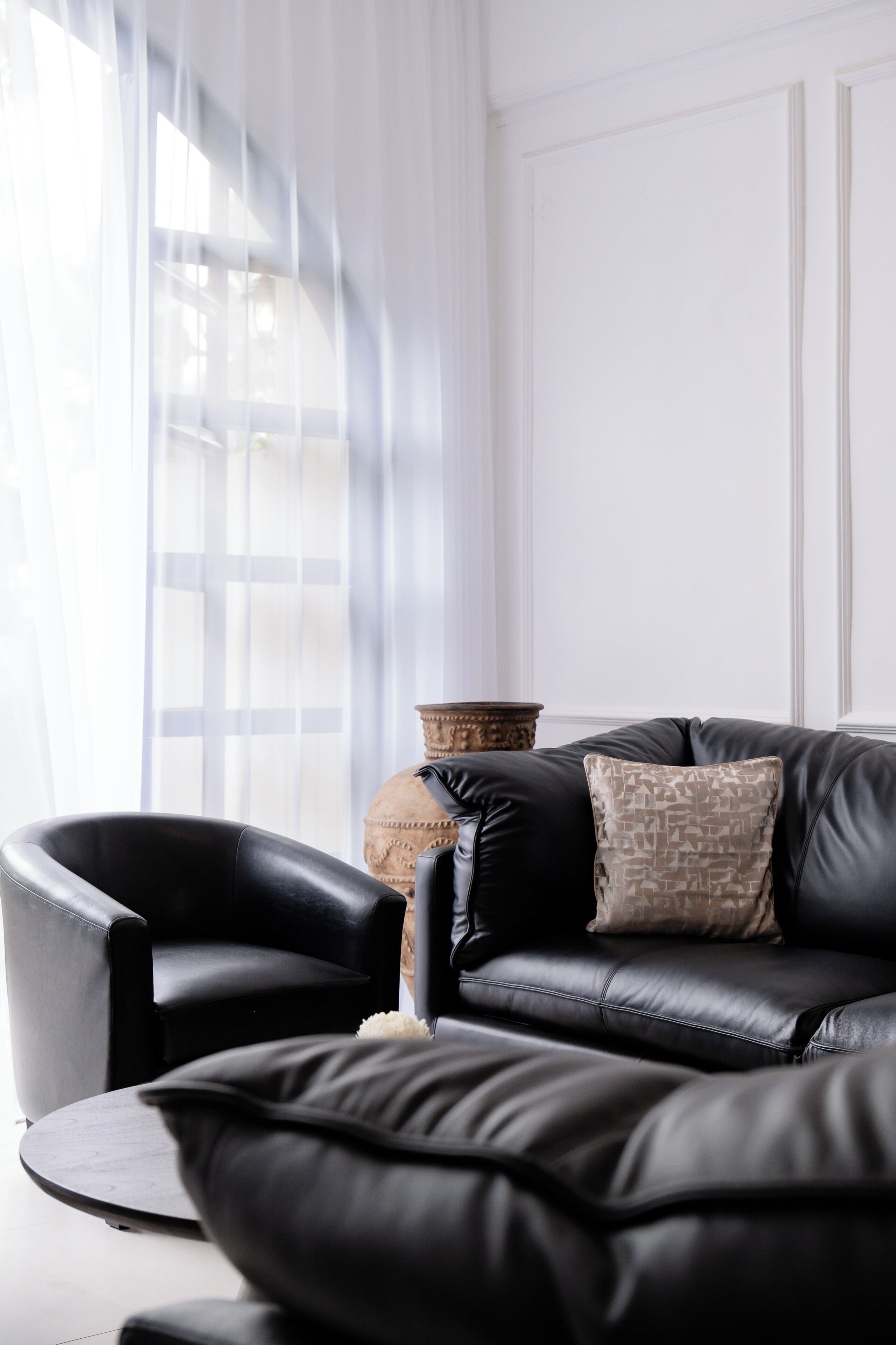Un salon moderne avec un canapé en cuir noir, une table basse ronde et un vase décoratif.