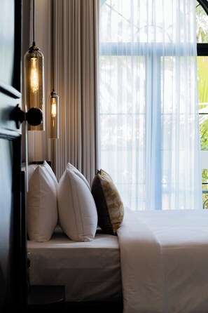Una cama con ropa de cama blanca, dos almohadas y una almohada decorativa, con una lámpara colgante.