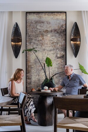 A dining area with a round table, chairs, and a large abstract painting on the wall. - Riviera Boutique Hotel (Ubud)
