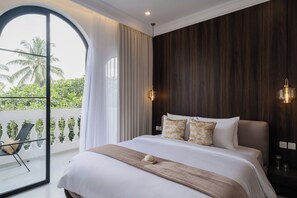 A hotel room with a large bed, a balcony with a chair, and a view of palm trees. - Riviera Boutique Hotel (Ubud)