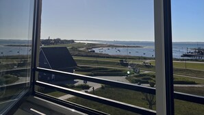 Uitzicht door een raam met blauwe lucht, een wateroppervlak en een verre kustlijn.
