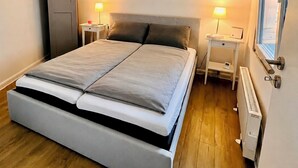 Een slaapkamer met een bed, nachtkastjes, een radiator en een raam.