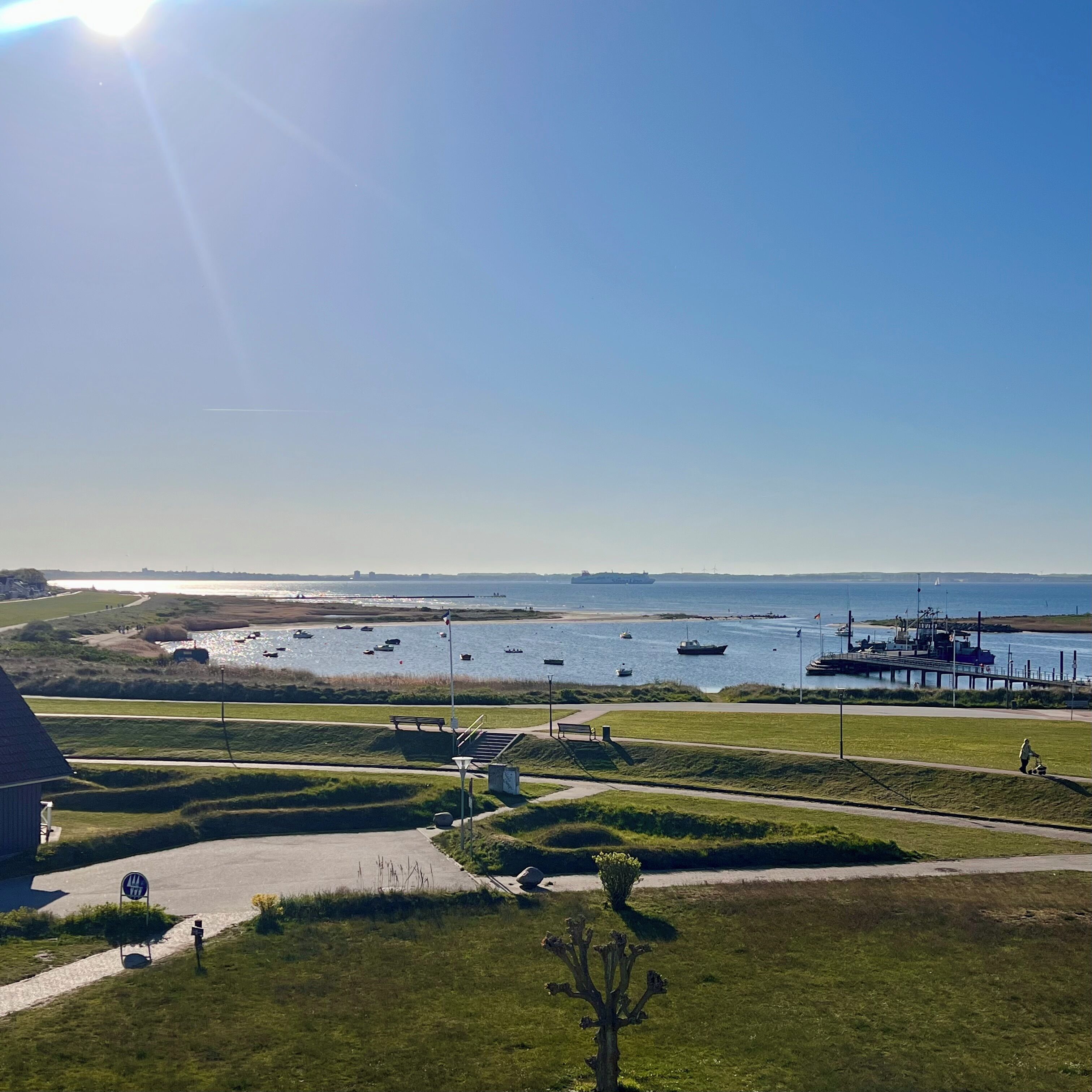 A coastal landscape with a clear sky, a grassy area with benches, and a body of water with boats.