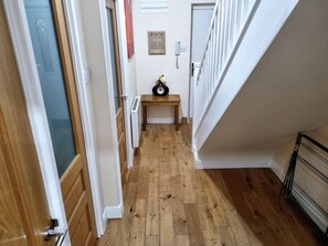 A hallway with wooden flooring, a small table with a vase, and a door with a frosted glass panel.