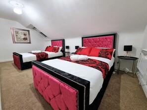 A bedroom with two beds, each with a red headboard and black accents, white bedding, and a small bedside table with a lamp.
