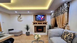 Una sala de estar con televisión, sofá, mesa de centro, chimenea y plantas decorativas.