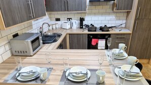 Una cocina moderna con una mesa de comedor lista para cuatro personas, equipada con microondas, tetera y diversos utensilios.