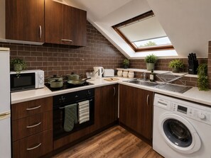 Une cuisine compacte dotée d’un four, d’un micro-ondes et d’un lave-linge encastrés, d’une lucarne et d’armoires en bois.