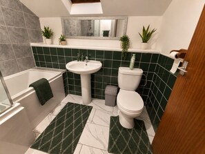 Une salle de bain avec une baignoire, un lavabo, des toilettes et des murs recouverts de carreaux verts.