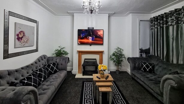 Olohuoneessa on kaksi sohvaa, takka, televisio ja kattokruunu.