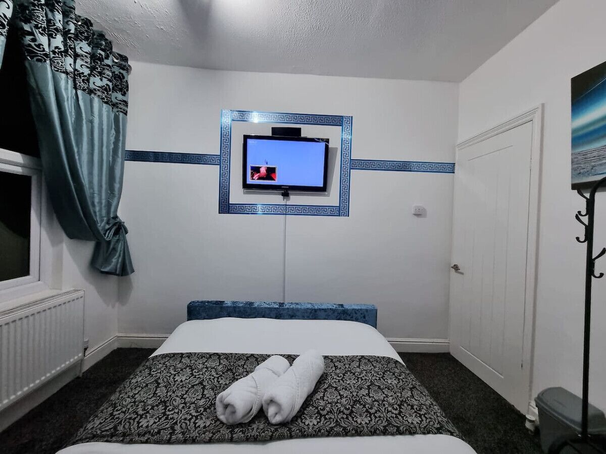 Une chambre d’hôtel avec un lit, un téléviseur fixé au mur, une fenêtre avec des rideaux et une porte.