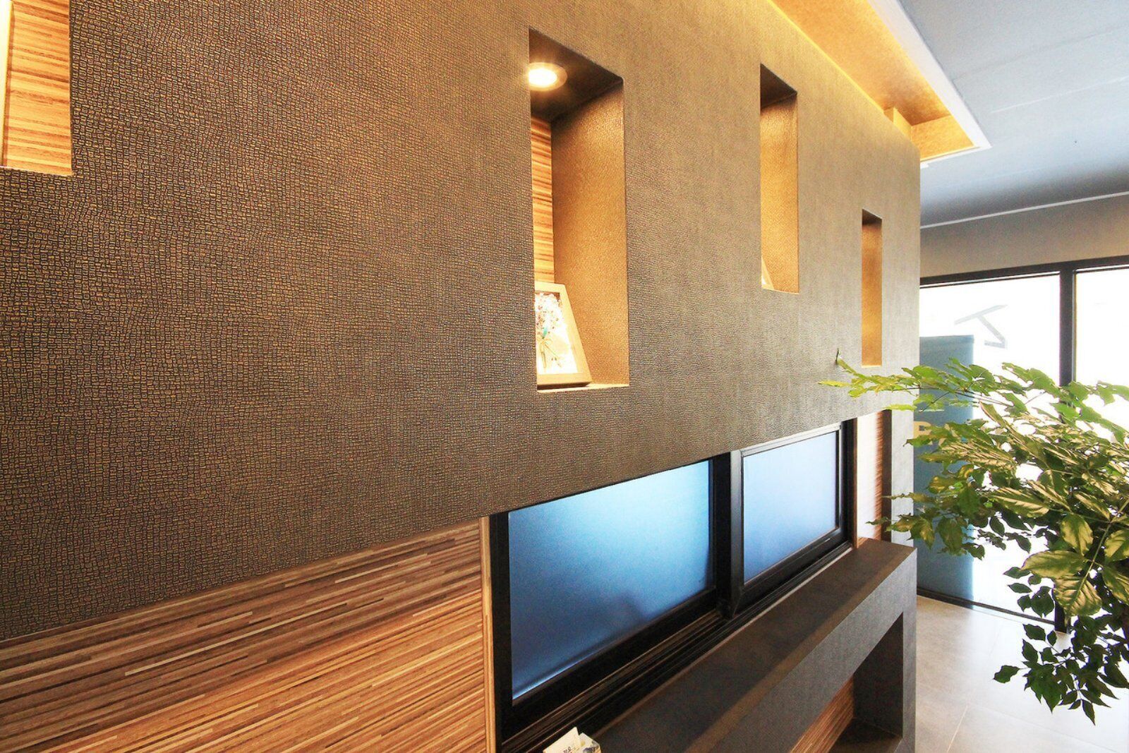 A modern interior with a textured wall, recessed lighting, and large windows.