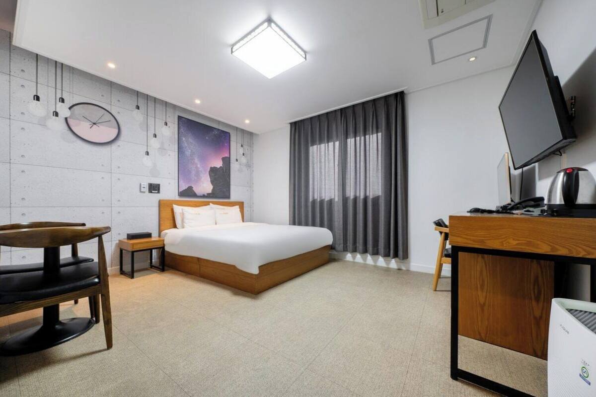 A modern hotel room with a bed, a desk, a chair, a TV, and a coffee maker.