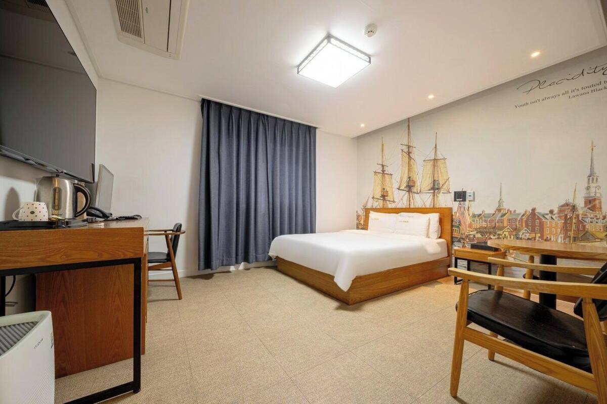 A hotel room with a bed, desk, chair, and a cityscape mural on the wall.