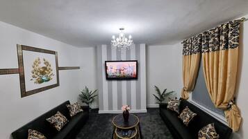 A living room with two black sofas, a TV, a chandelier, and a patterned curtain.