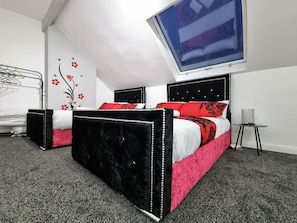 A bedroom with two beds, a skylight, a wall decoration, and a small table.